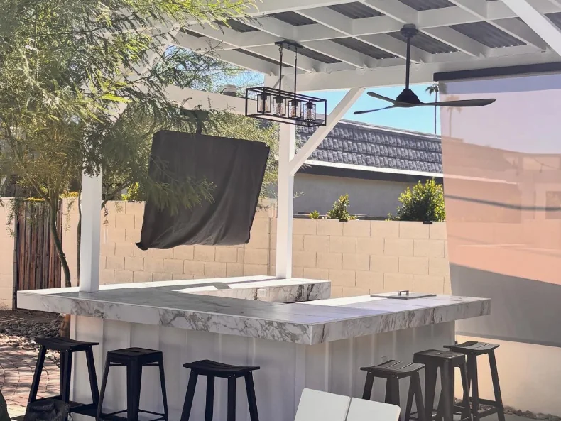 After: backyard bar under a white pergola with new counters, lights and a ceiling fan