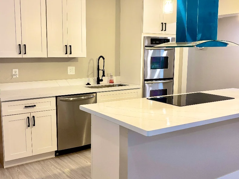 After: white shaker kitchen with a white quartz island and a teal range hood
