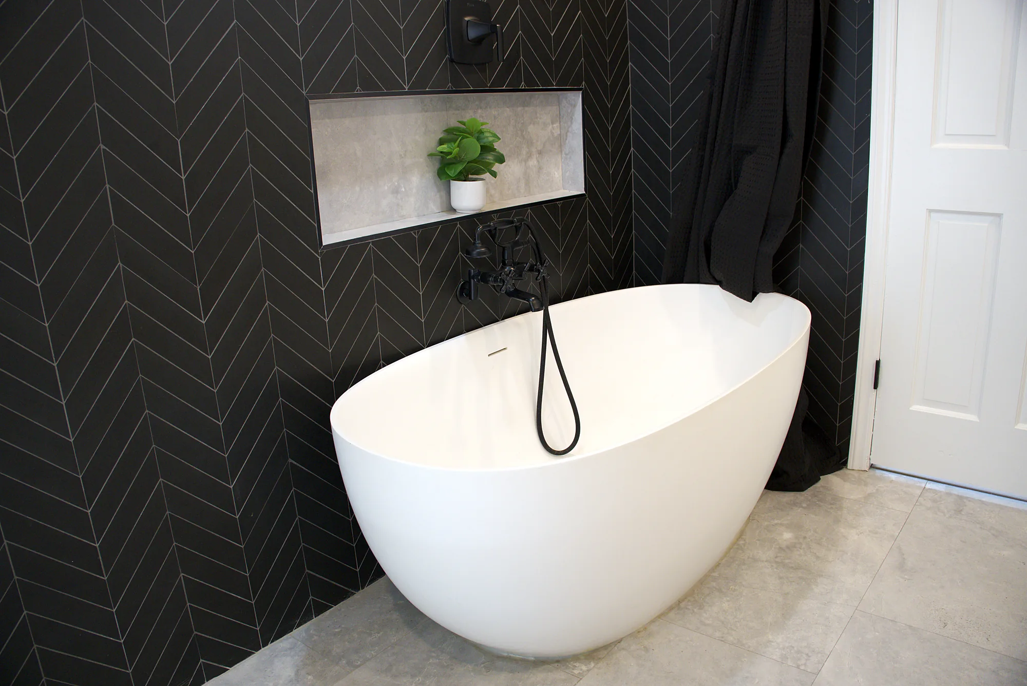 Freestanding tub against black herringbone tile, finished on the same takeover job