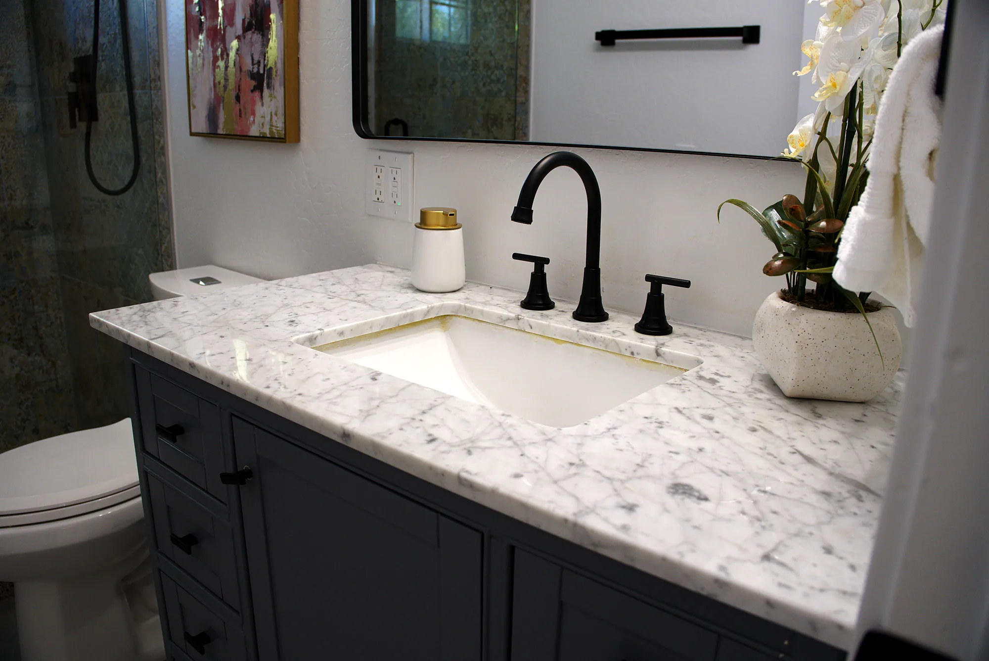 Gray vanity with a white marble look countertop and black faucet