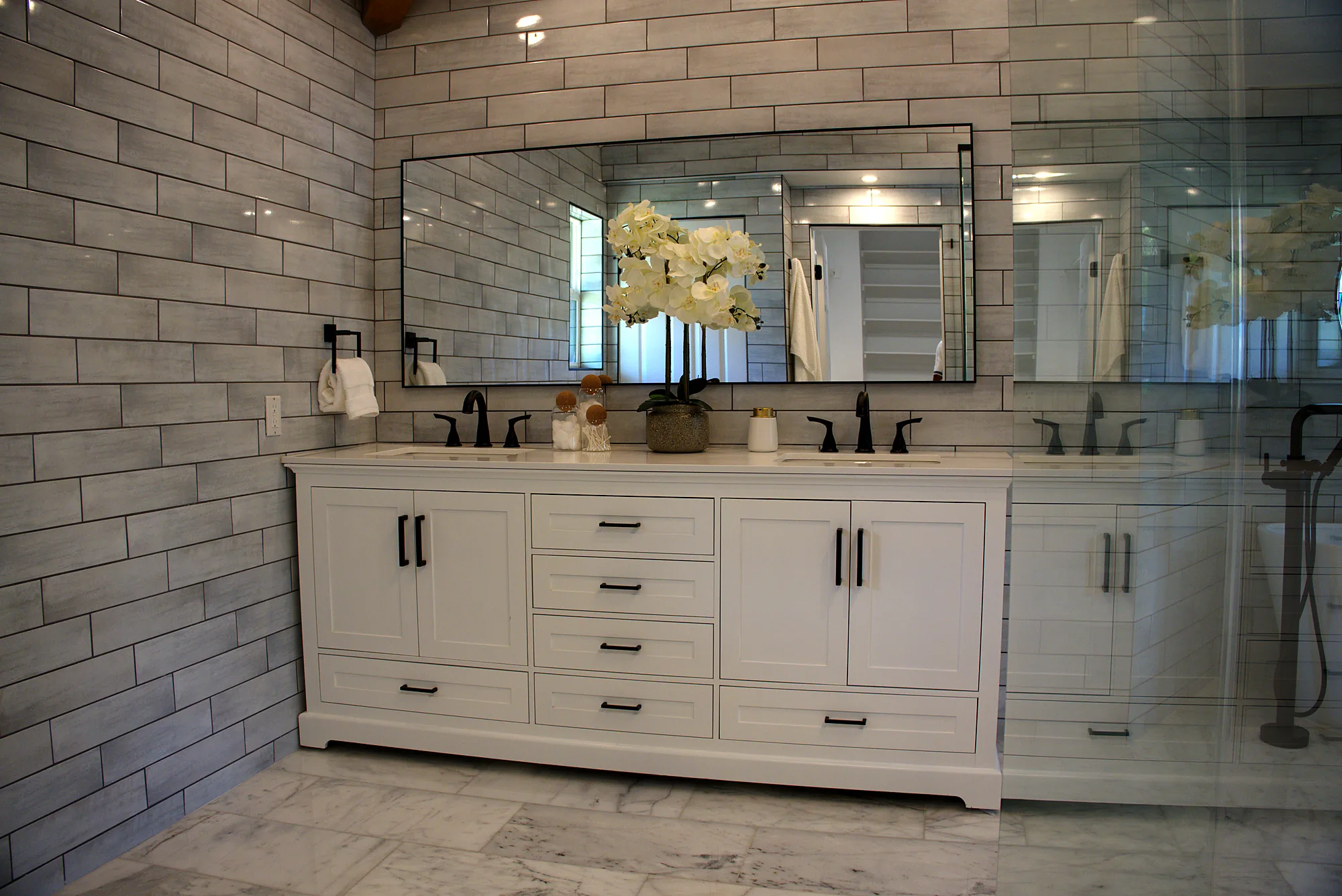 White double vanity with black faucets and a long mirror in a primary bath