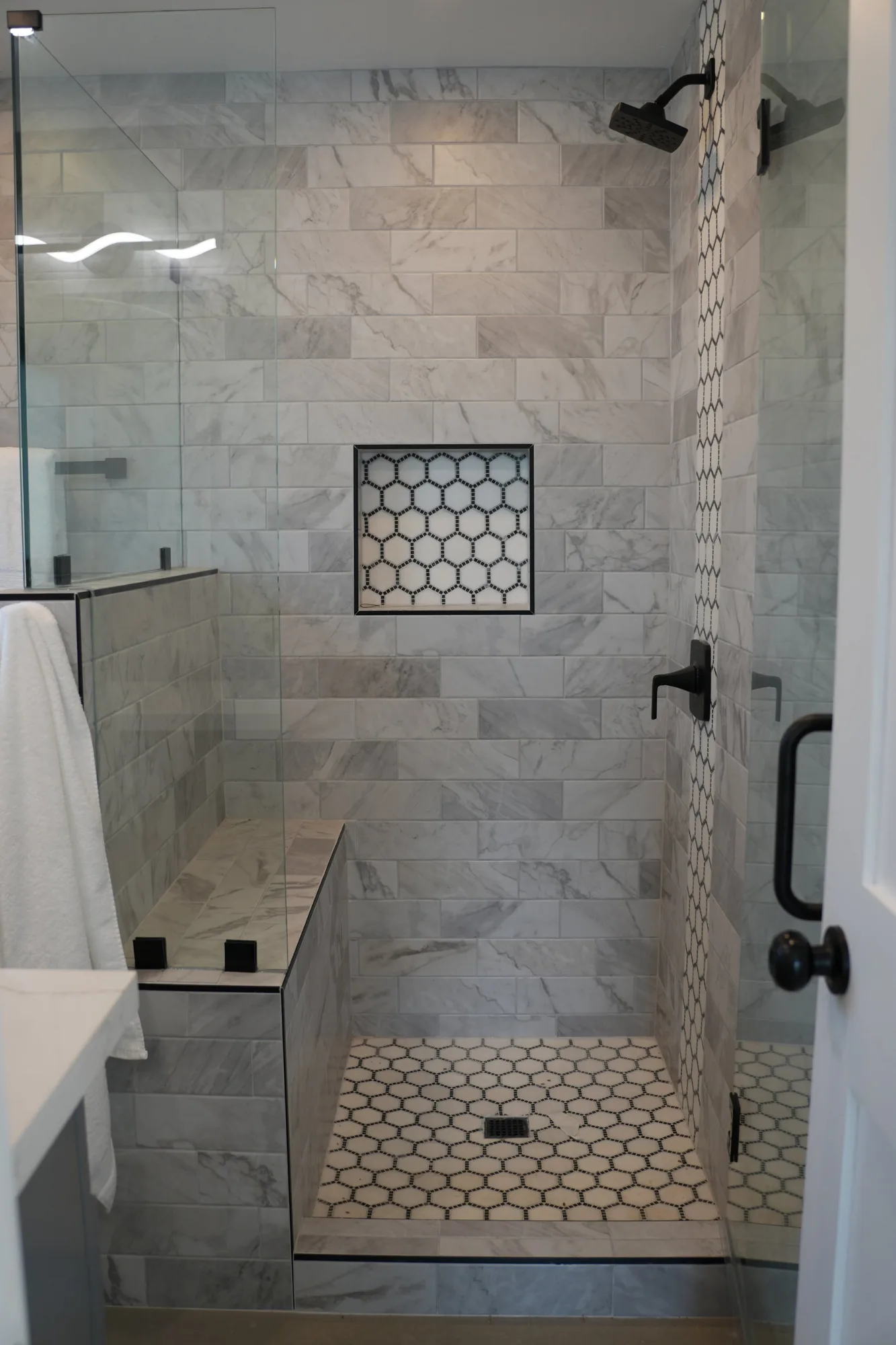 Walk in shower with a tiled bench, glass panels and a hexagon tile niche